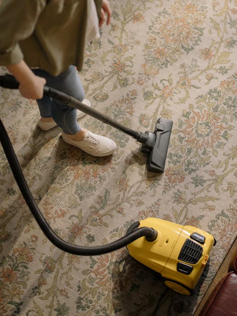 A professional cleaner from Harrow Carpet Cleaners dressed in full protective gear, including a white coverall suit, gloves, mask, and shoe covers, uses a portable steam cleaning machine equipped with